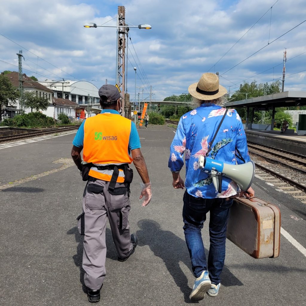 Zwei Männer - einer mit Koffer - laufen auf einem Bahnsteig entlang