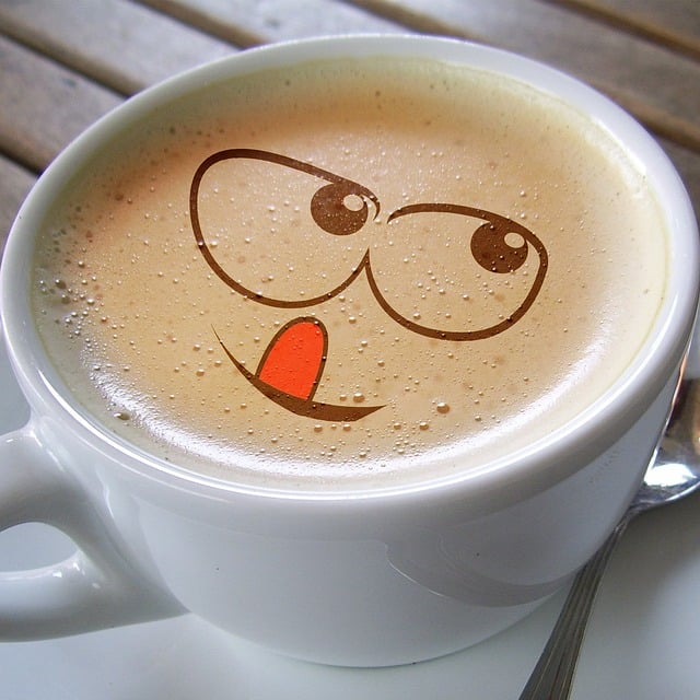Tasse Kaffeee mit Schaum und einem Emoji, das sich die Lippen leckt