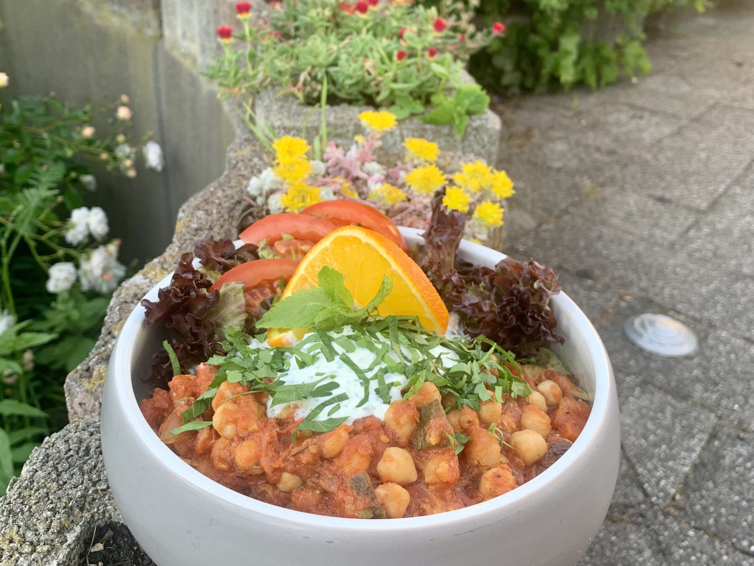 In einer Schale ist ein Gericht mit Kichererbsen, Salat und Orangenscheibe angerichtet