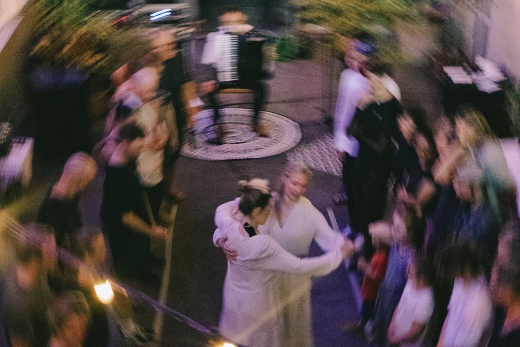 Verschwommenes Foto von zwei tanzenden Frauen in weiß, um sie herum stehen Menschen