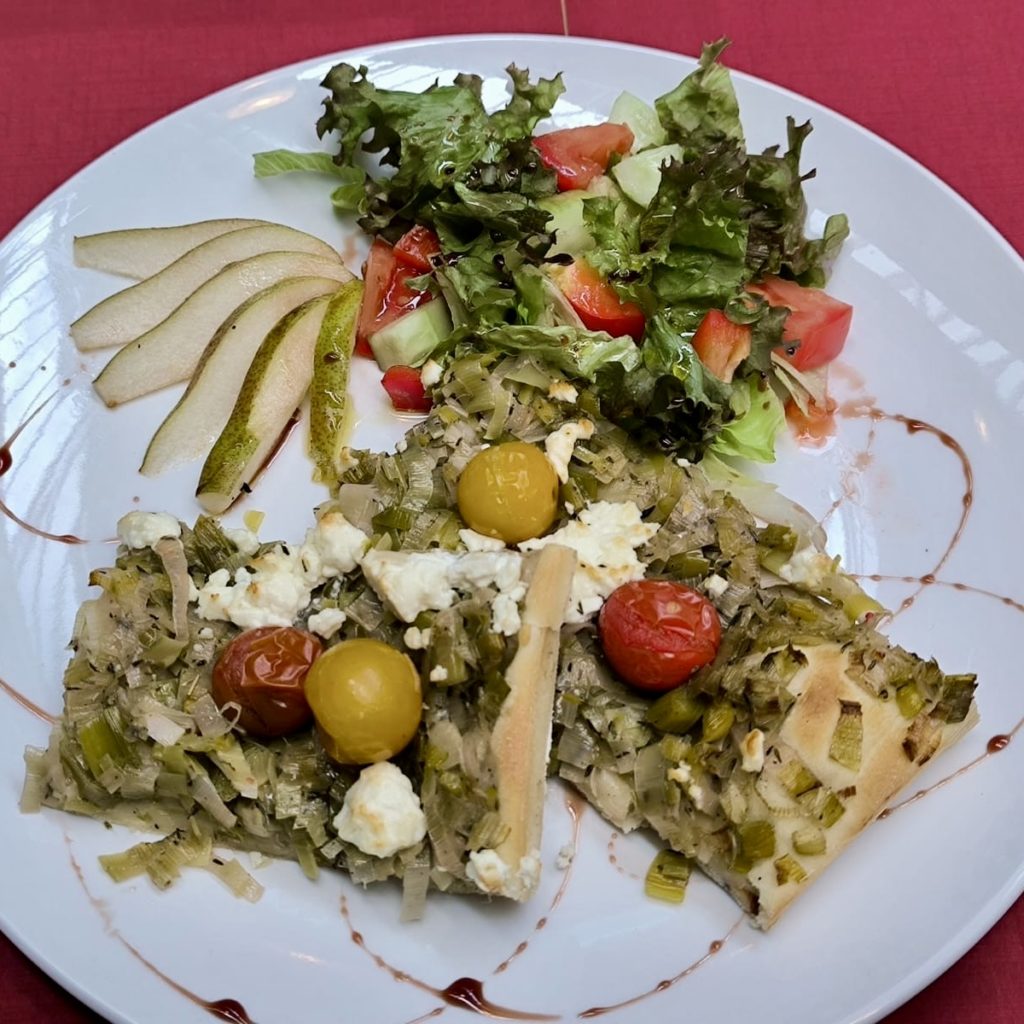 Ein weißer Teller mit einem bunten Gericht und Salat steht auf einer roten Tischdecke
