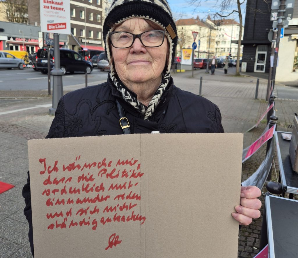 Ältere Frau hält ein Pappschild in die Höhe.