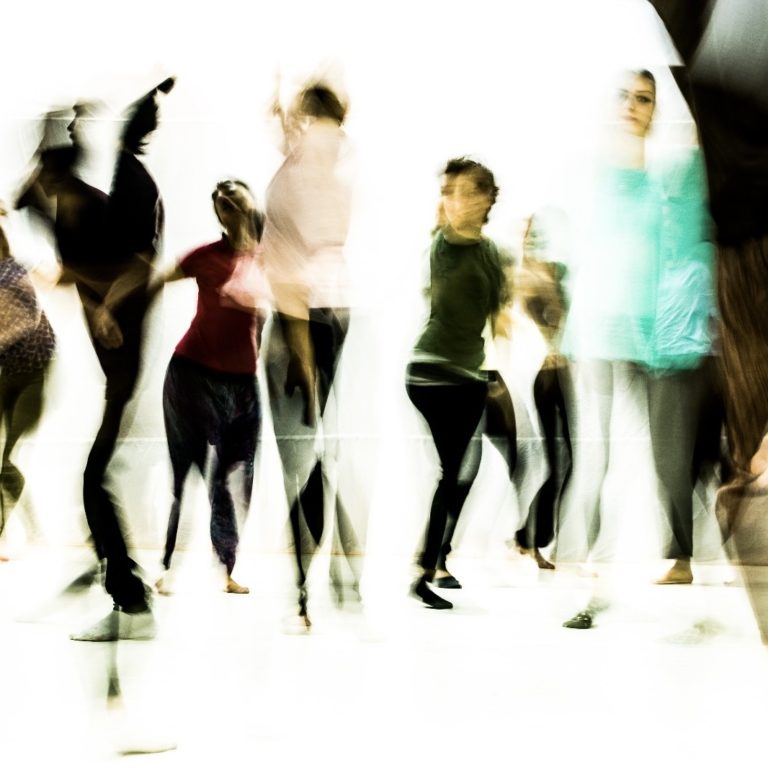 Vor einer weißen Fläche tanzen einige Menschen.