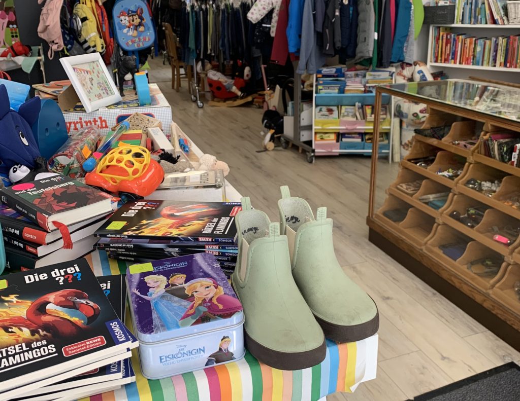Ein Paar grüne Gummistiefel stehen in einem Laden, in dem gebrauchtes Spielzeug angeboten wird.