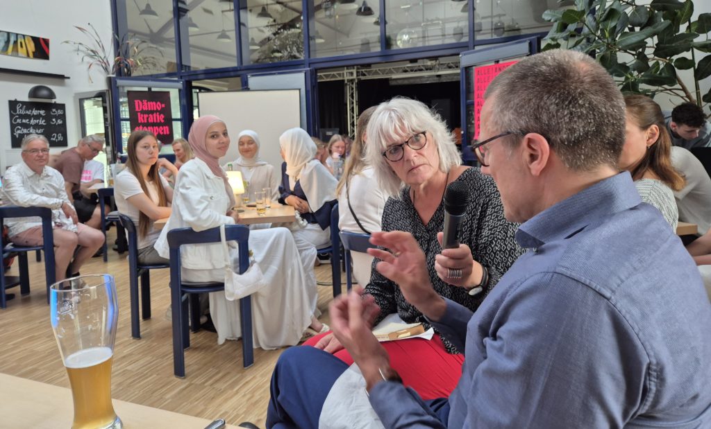 In einem Raum mit vielen Menschen hält eine Frau einem Mann das Mikrophon hin