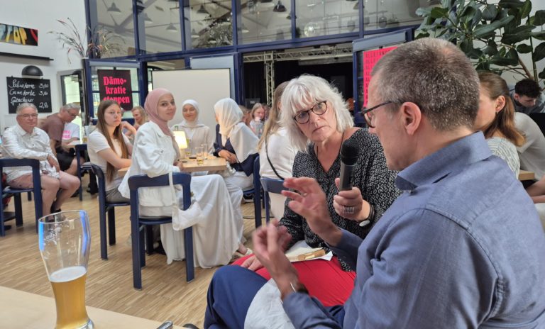 In einem Raum mit vielen Menschen hält eine Frau einem Mann das Mikrophon hin