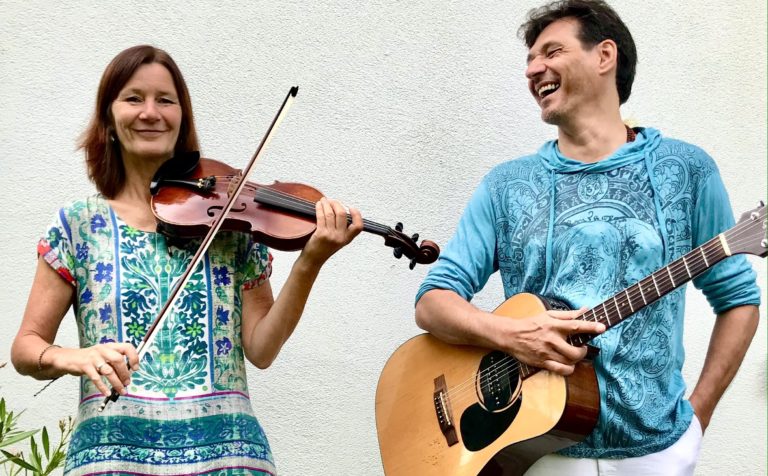 Eine Frau an der Geige und an Mann an der Gitarre lachen