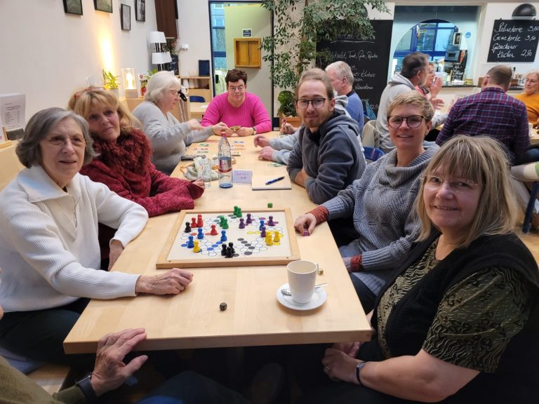 Viele Menschen sitzen um einen Tisch mit einem Brettspiel darauf