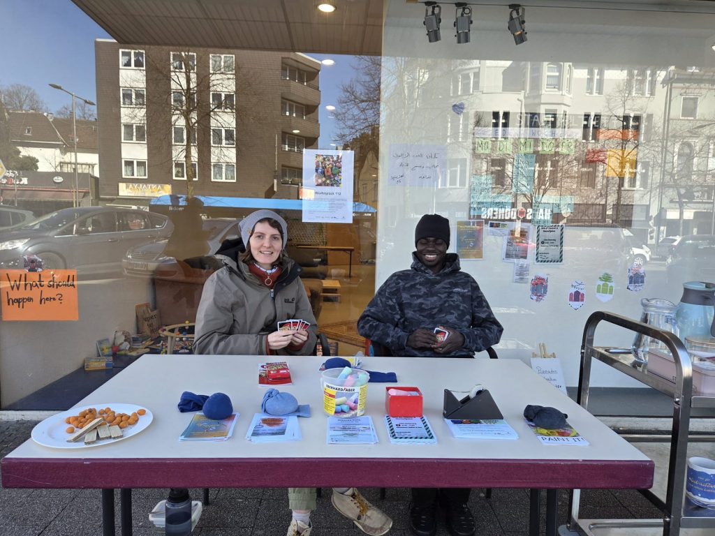 An einem Tisch mit Flyer darauf sitzen eine Frau und ein Mann.