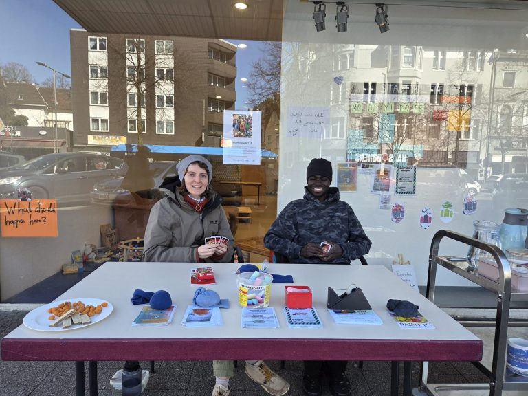 An einem Tisch mit Flyer darauf sitzen eine Frau und ein Mann.